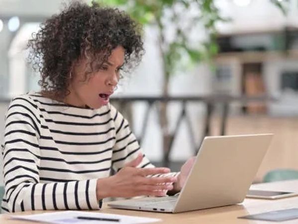 Woman sitting at her computer shocked by what she sees on the computer screen.