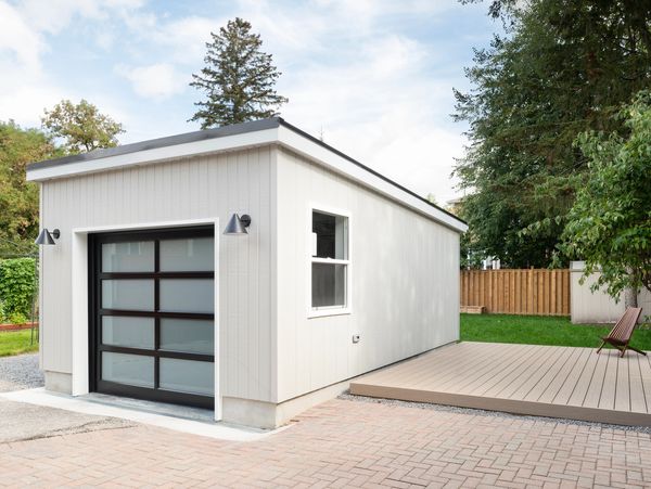 Modern white garage with frosted glass door and wooden deck beside it.