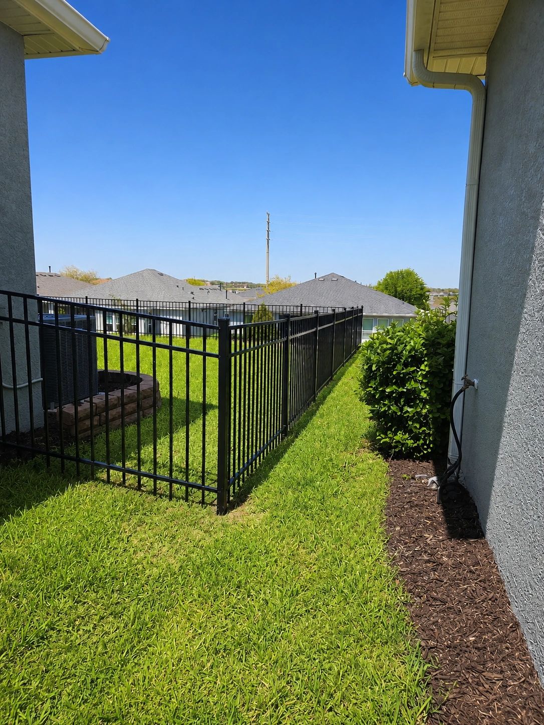 Yard with black metal fence and green grass under clear blue sky.