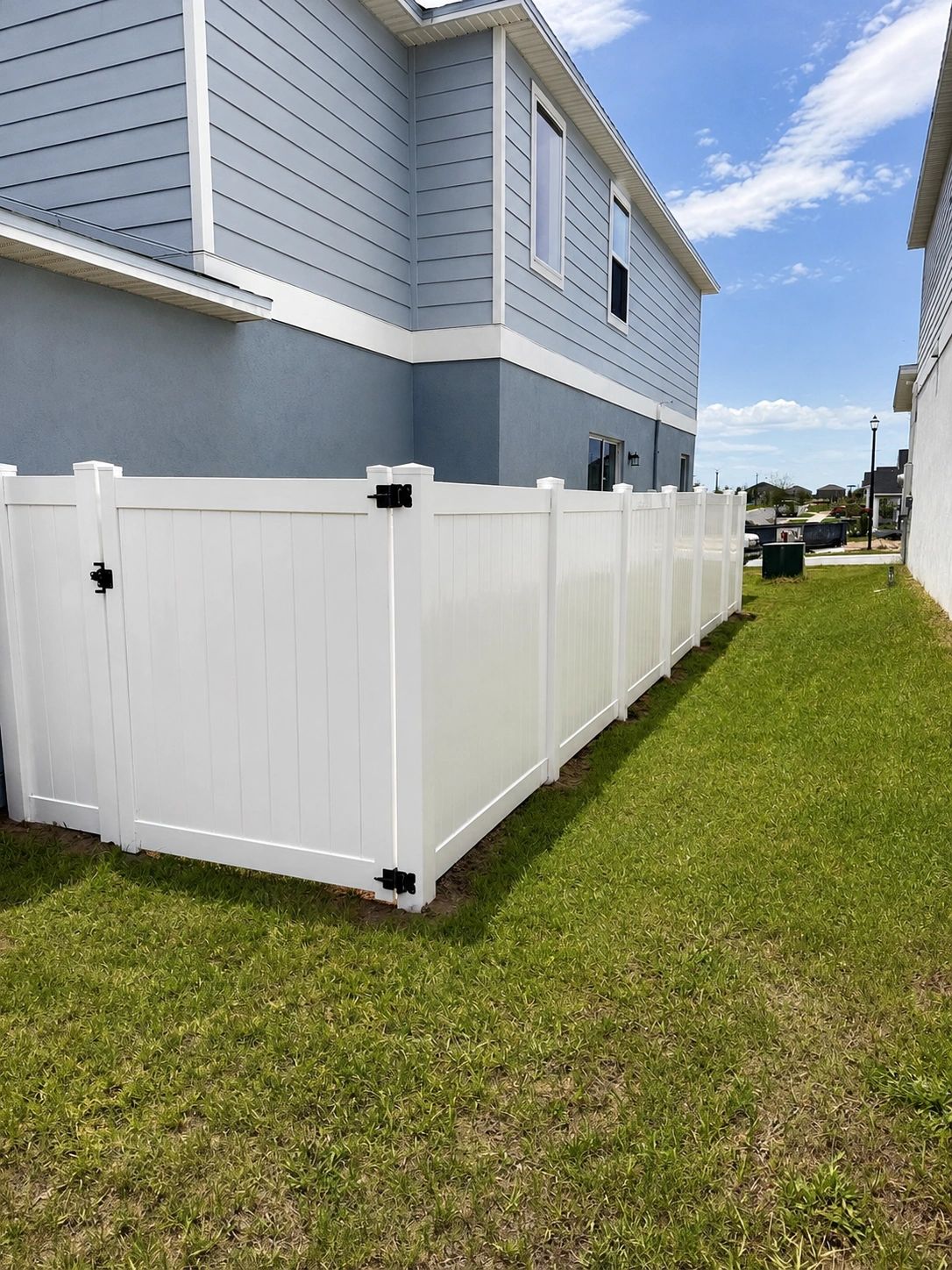White vinyl fence around a corner of a house with green grass.