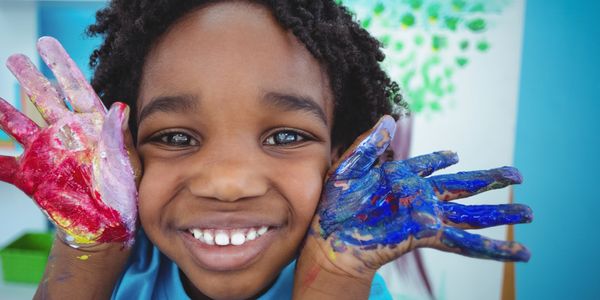 Smiling child with colorful paint on hands.