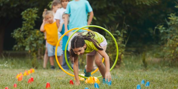 Children playing an outdoor obstacle course with hoops and cones.