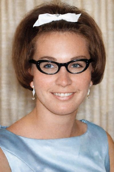 Portrait of a woman with glasses and a white hair bow smiling.