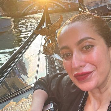 Woman taking a selfie on a gondola with a sunset bridge in the background.