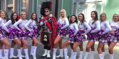 Group of women in plaid skirts with one man in traditional Scottish attire.