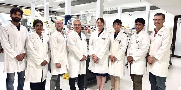 A diverse group of nine scientists in lab coats standing in a laboratory.