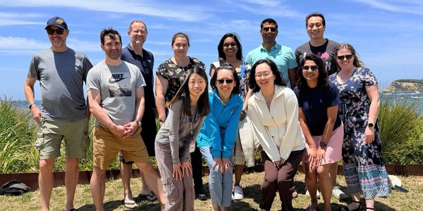 A group of people posing outdoors on a sunny day near the coast.