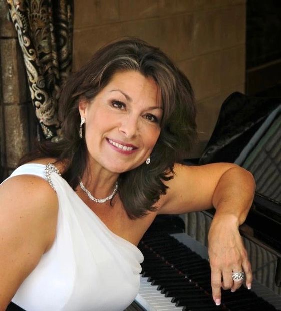 Woman in white dress sitting at piano and smiling.