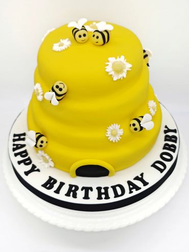 A Beehive shaped cake with little flowers and bees all over it.