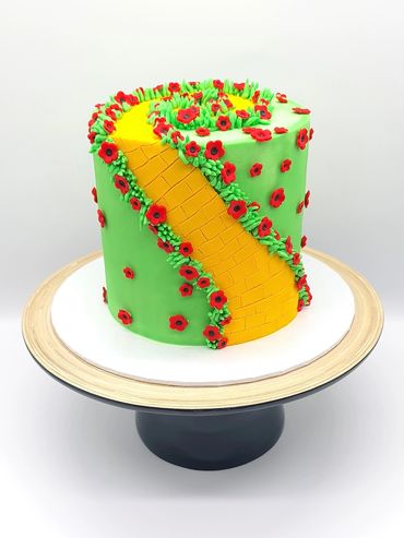 Green cake with the Wizard of Oz yellow brick road twisting around the cake. Red poppies along road