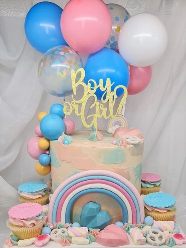 Pink and blue cake for a gender reveal party. Rainbow, balloons, sweets and cupcakes around the cake