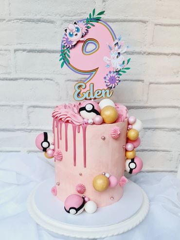 Pink cake in a Pokemon theme. Pink pokeballs on cake. Pokemon card topper. Pink icing and sprinkles.