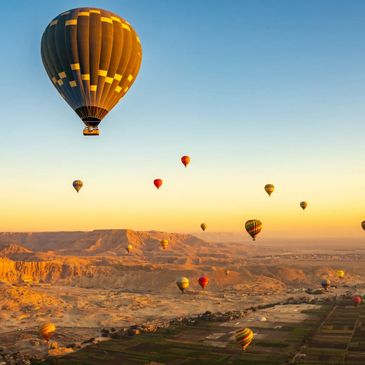 Multiple colorful hot air balloons floating over a desert landscape at sunrise.