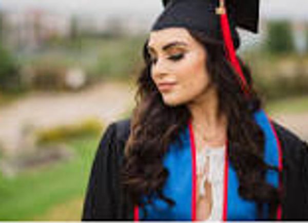 Young woman in graduation attire looking down thoughtfully.