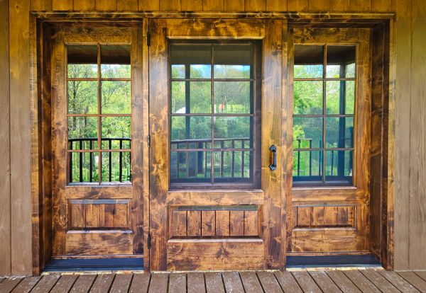 Rustic wooden patio doors with glass panes opening to a green garden.