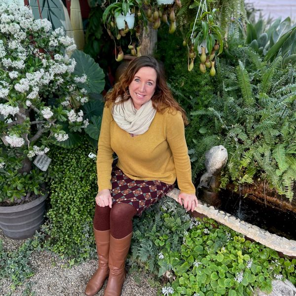 Woman sitting by a lush garden pond with various plants.