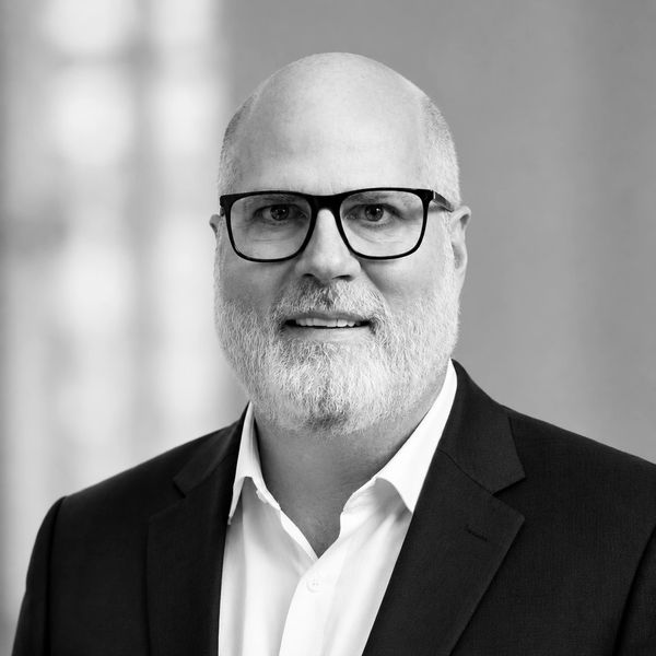 Black and white headshot of a bald man with glasses and beard.