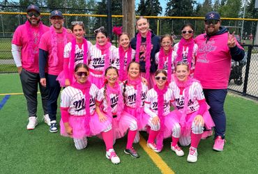 Youth softball team and coaches wearing pink uniforms and accessories on the field.