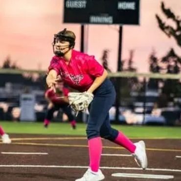 Softball pitcher in pink uniform delivering a pitch on the field.