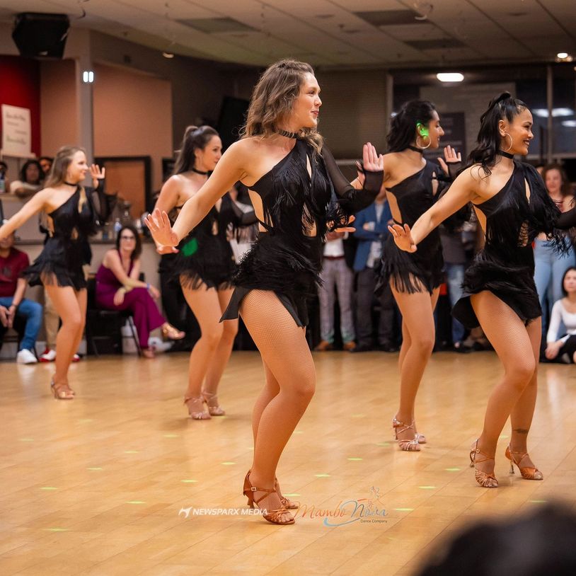 A group of women dancing in black fringe dresses on a wooden floor.