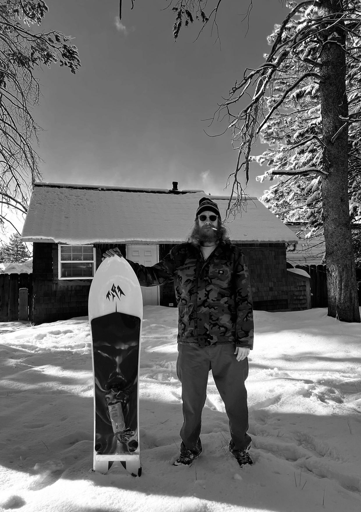 Man with snowboard standing in the snow near a cabin.