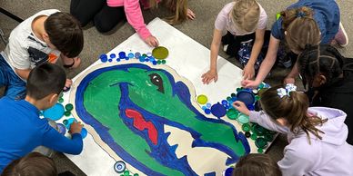 Children gather around a colorful alligator artwork.