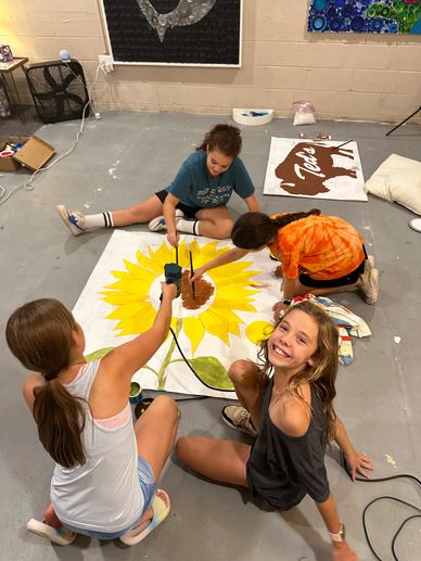 Kids painting a large sunflower artwork on the floor.