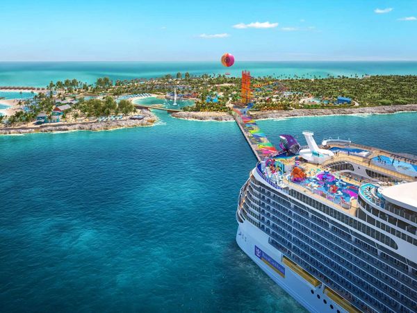 A large cruise ship docked at a colorful tropical island resort with a hot air balloon overhead.