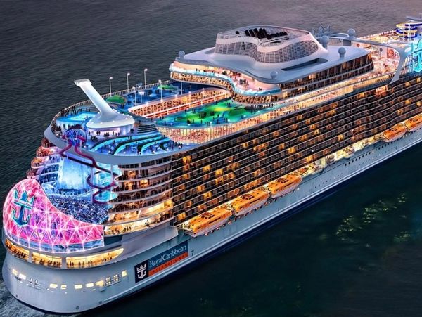 A brightly lit Royal Caribbean cruise ship at night with pools and a waterslide.