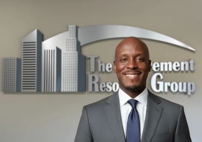 A businessman smiling in front of a corporate logo wall.