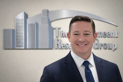 Professional man in a suit smiling in front of a business logo.