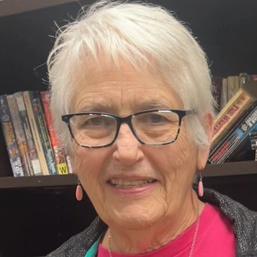 Smiling elderly woman in glasses and pink shirt.