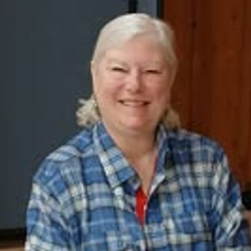 Smiling woman in blue plaid shirt sitting at a table.