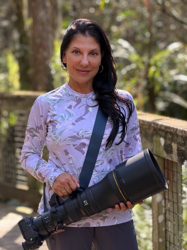 Woman holding a large telephoto camera lens outdoors.