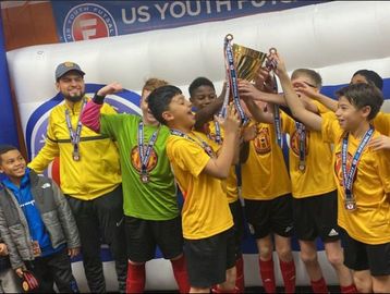 Youth soccer team celebrates winning a trophy indoors.