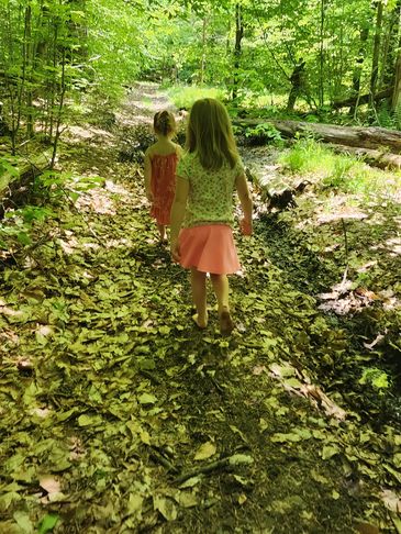 Two young girls walking barefoot on a leafy forest path.