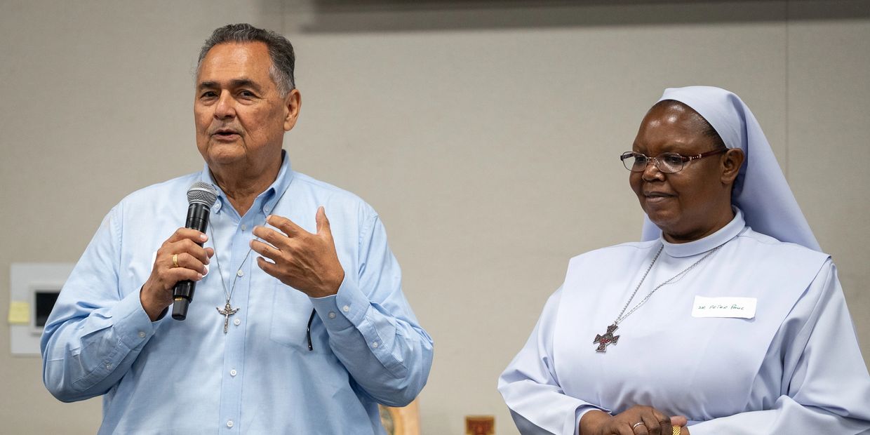 Man speaking with a microphone, woman nun listening.