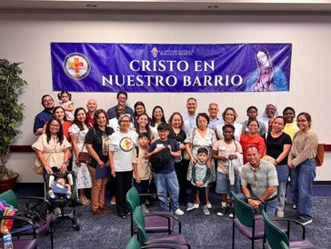 Group photo of diverse people under a banner reading Cristo en Nuestro Barrio.