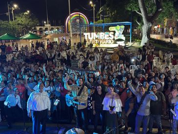 Night crowd gathering in Tumbes, Peru, with a glowing sign.