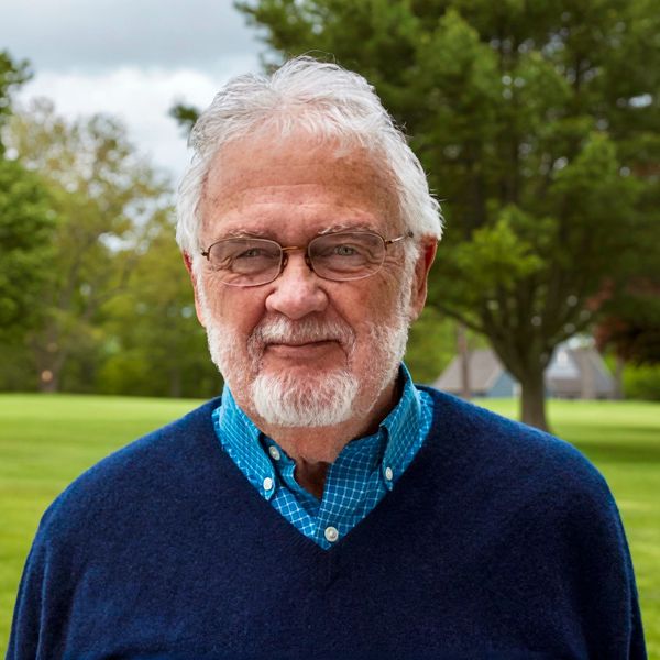 Elderly man with white hair and glasses smiling outdoors.