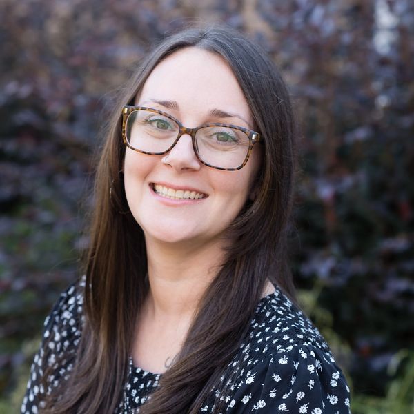 Smiling woman with glasses and long brown hair outdoors.