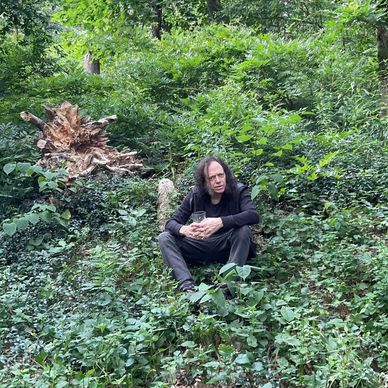 Man sitting in a lush green forest clearing.