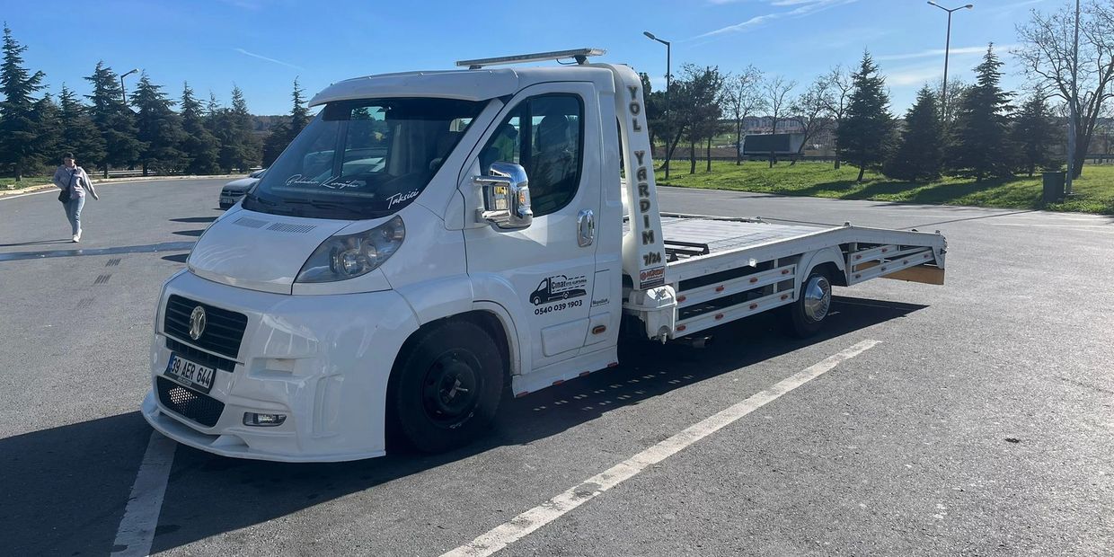White flatbed tow truck parked in an empty lot under a clear blue sky.