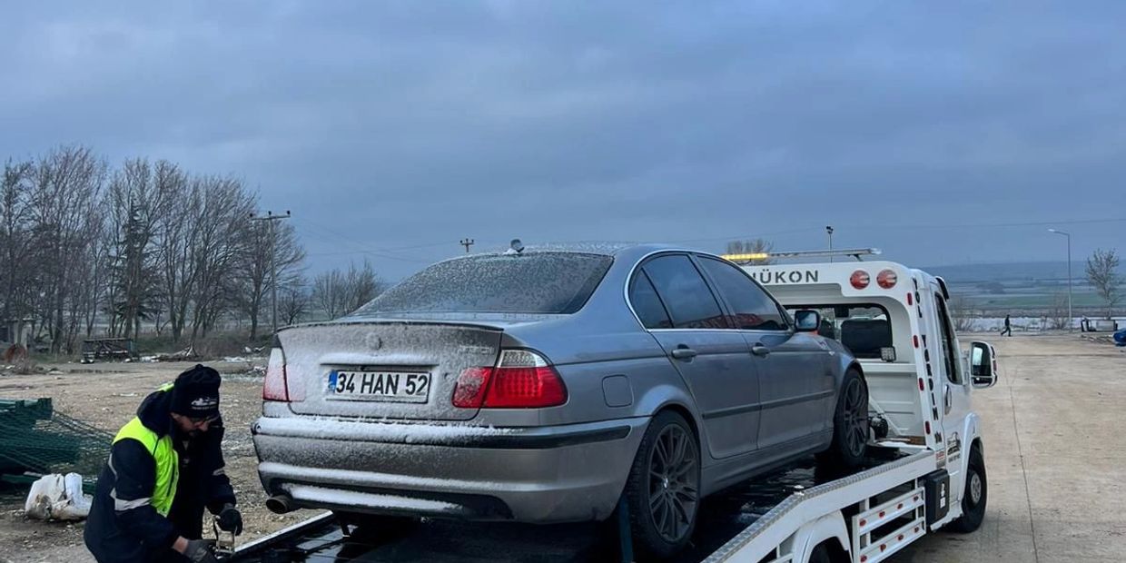 A dusty silver car being loaded onto a white tow truck by a worker.