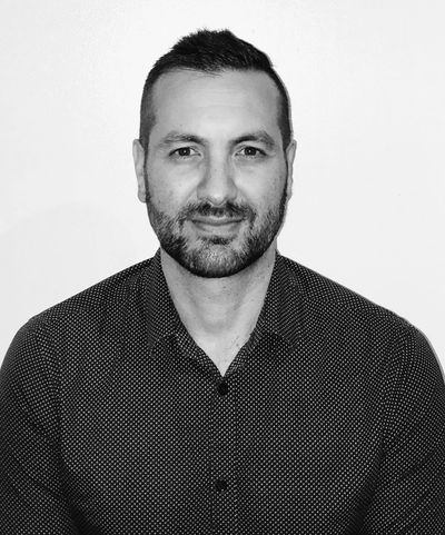 Black and white portrait of a man with short hair and a beard, wearing a patterned shirt.