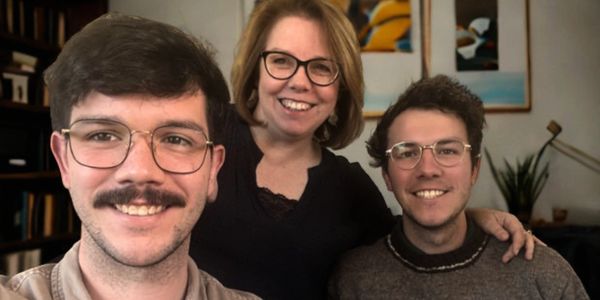 Three people smiling indoors, two men and one woman with glasses.