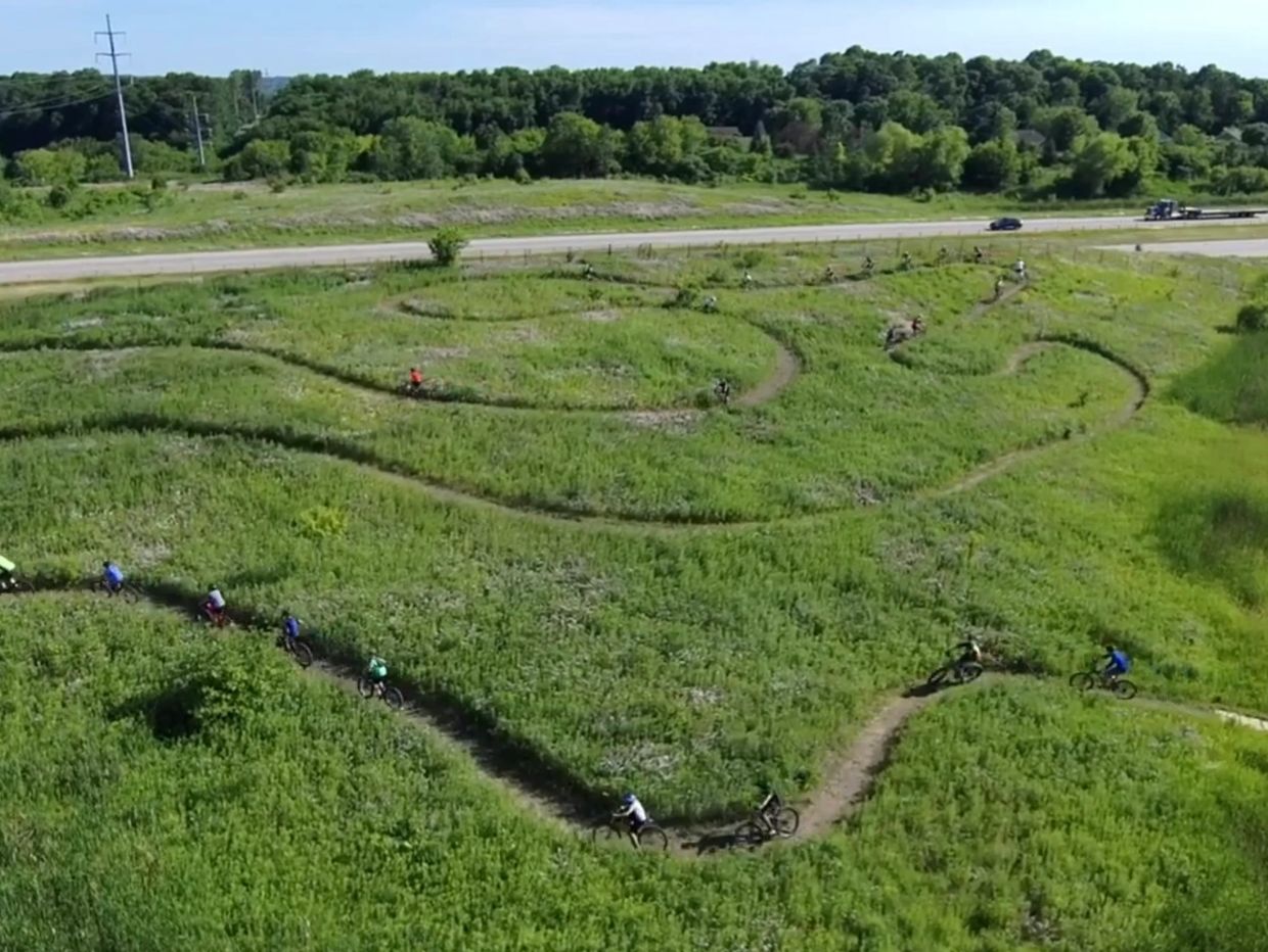 Cyclists riding mountain bikes on winding trails through green fields.