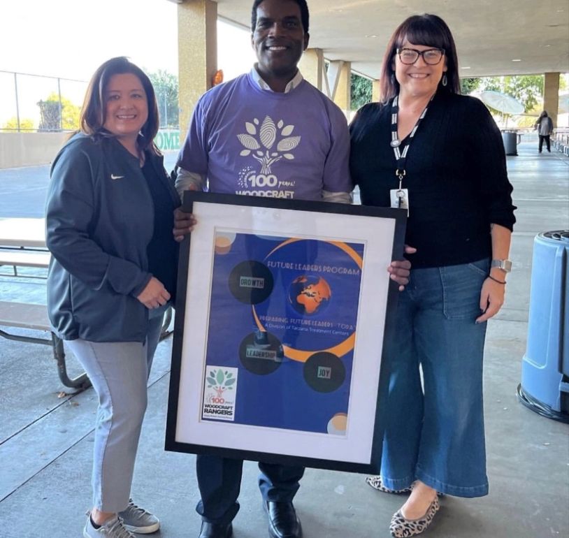 Three people holding a framed poster for Future Leaders Program.