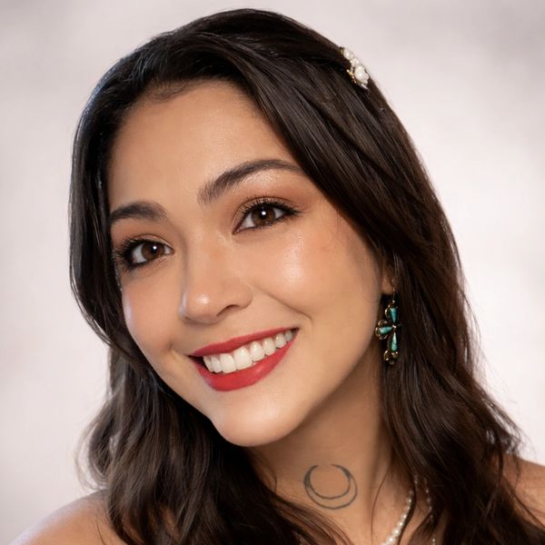 A smiling young woman with red lipstick and a crescent moon tattoo on her neck.