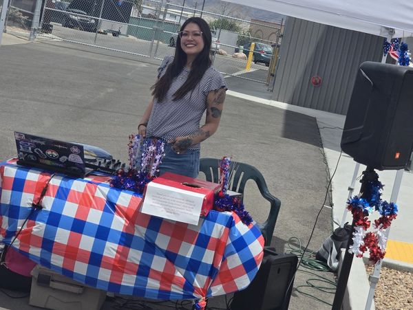 Smiling woman standing behind a decorated table outdoors under a canopy.
